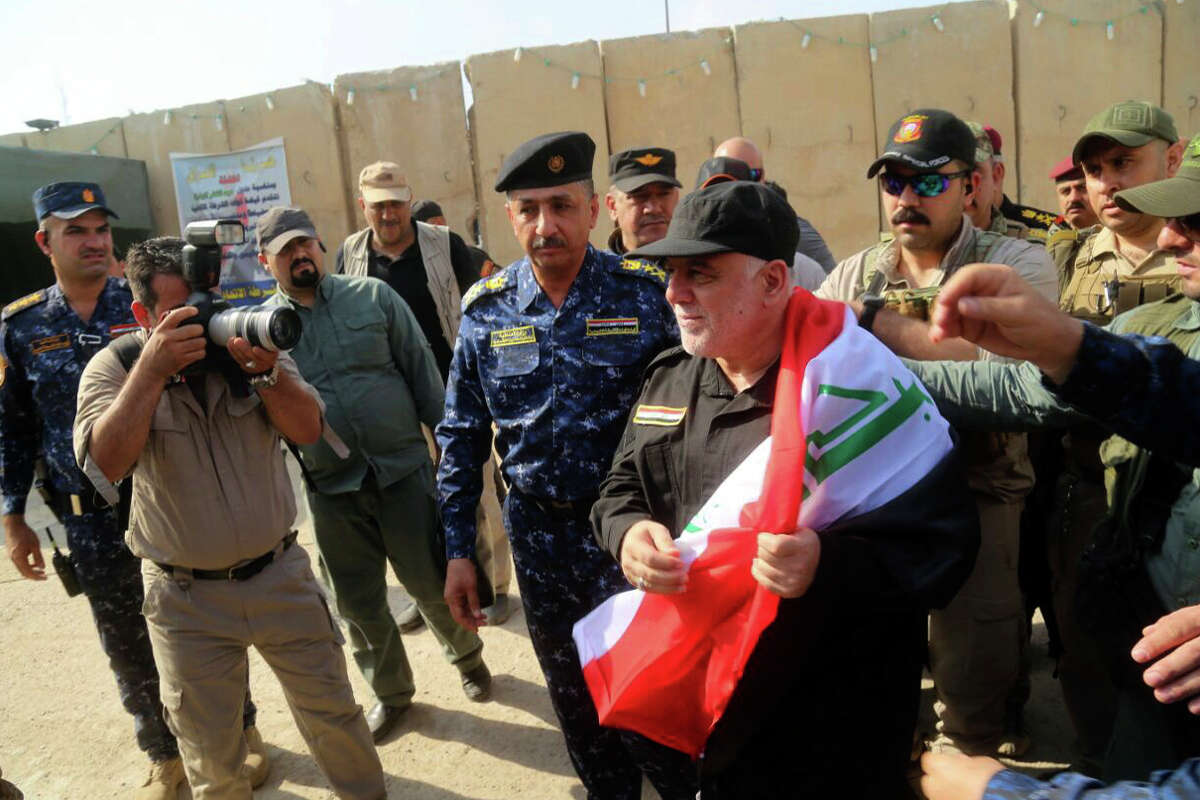 Iraq's Prime Minister Haider al-Abadi, center, holds a national flag upon his arrival to Mosul, Iraq, Sunday, July 9, 2017. Backed by the U.S.-led coalition, Iraq launched the operation to retake Mosul from Islamic State militants in October. (Iraqi Federal Police Press Office via AP)
