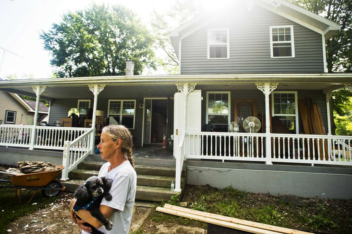 Peggy Sue Ginter stands in her front yard with her dog, Jesse, as a group from Team Rubicon works to gut the inside of her home, which was severely damaged by recent flooding, on Tuesday, July 11, 2017 on Atwell Street near Poseyville Road.