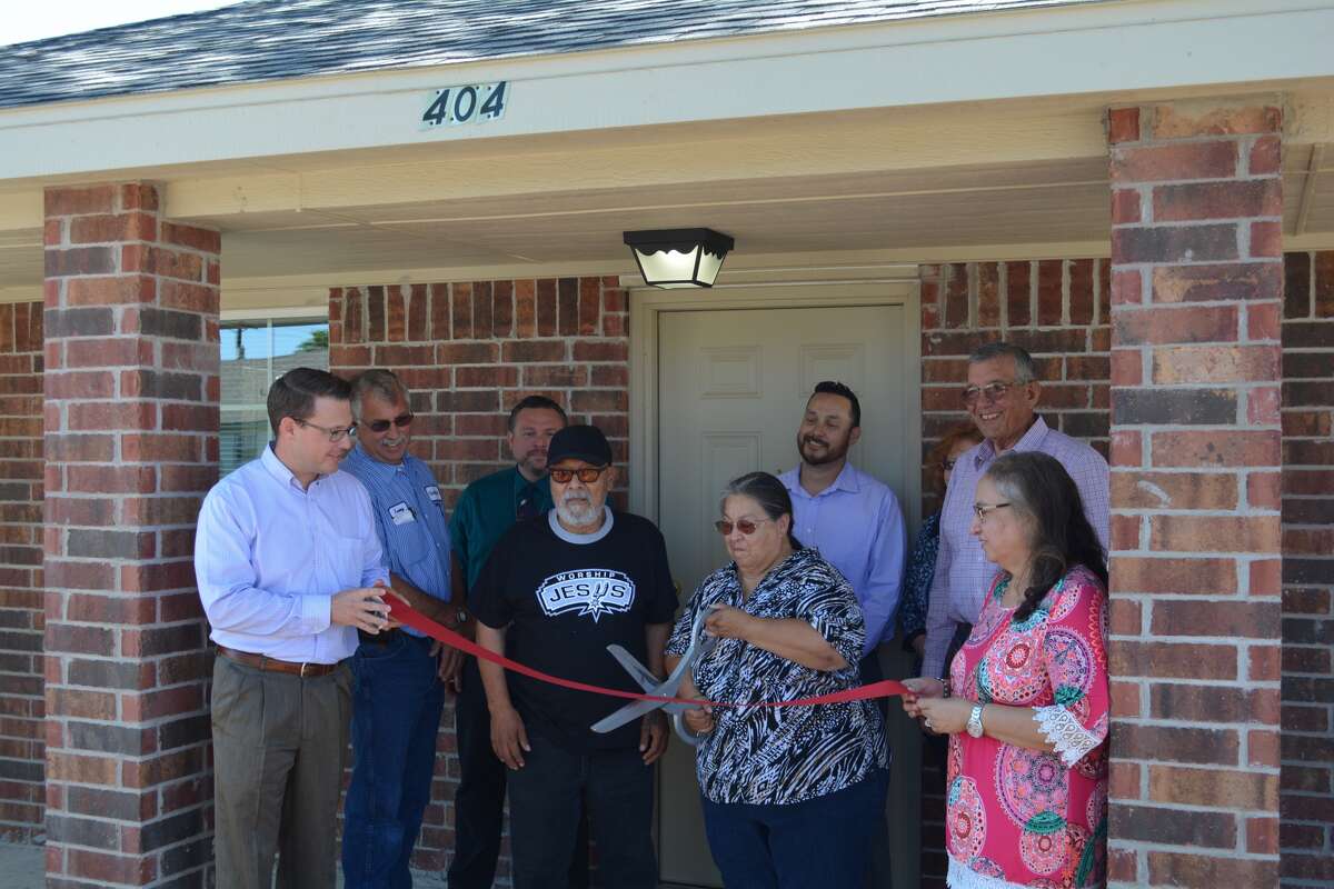 With City Manager Jeffrey Snyder (left) and City Secretary Belinda Hinojosa hold a ribbon for Abraham and Rosa Martinez to cut Wednesday outside the couple’s new home at 404 E. Third St. They were one of three families Wednesday to receive keys and take possession of newly constructed residences.