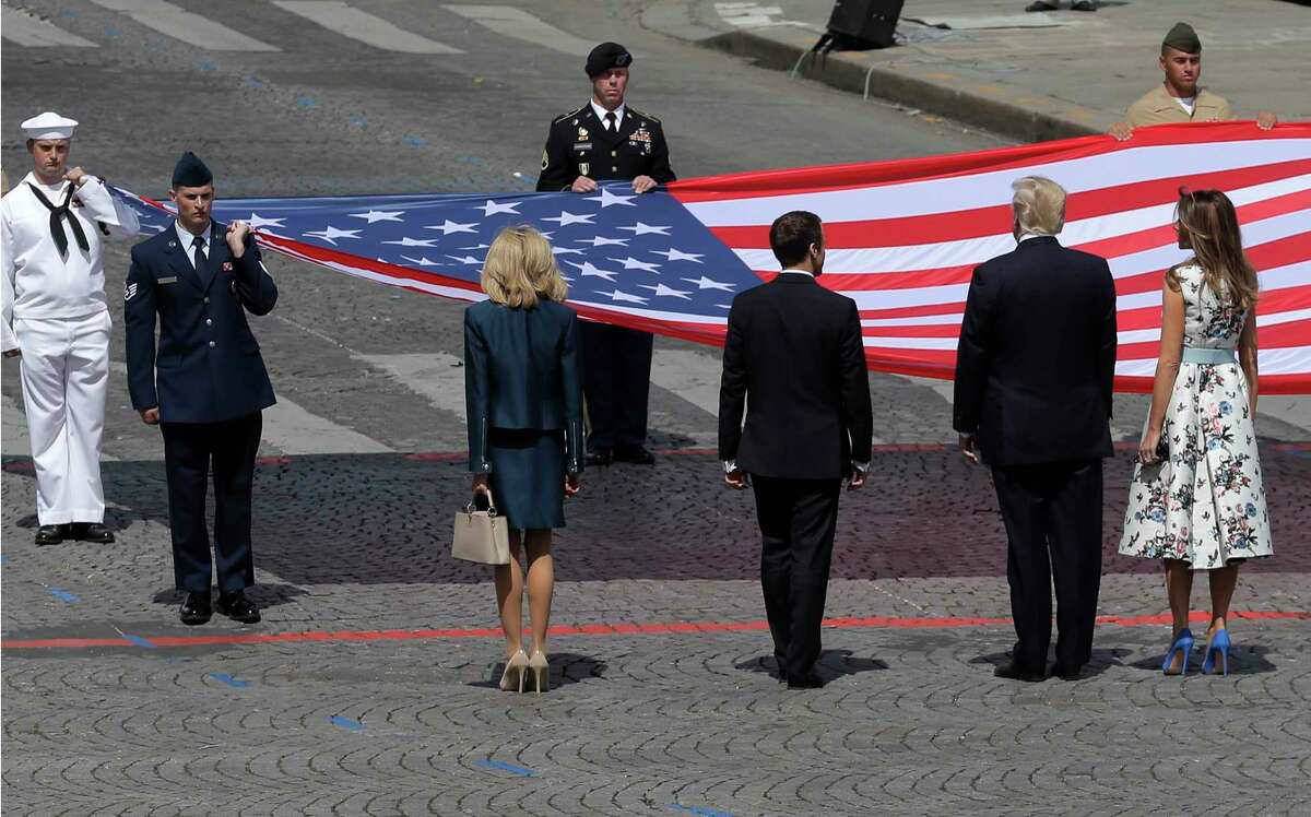 French President Emmanuel Macron, fourth from left, and his wife, Brigitte, to his left, stand with President Donald Trump and first lady Melania Trump as an American flag is presented during a Bastille Day parade in Paris.﻿