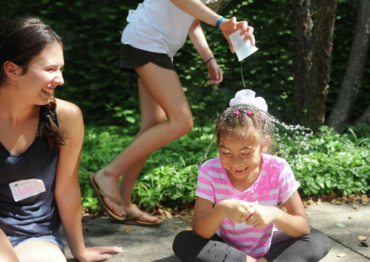 Rising third-grader Stephanie Molina gets water dumped on her head by volunteer rising senior Katie McClymont during a game of “Drip, Drip, Drop” during outdoor snacktime at the Greenwich Academy Talent Enrichment camp.