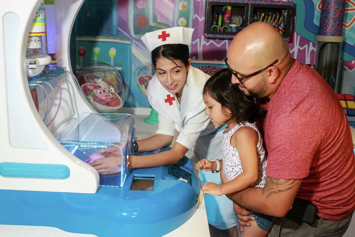﻿Jonathan Vargas and his daughter, Adalyn, 3, watch as ﻿Natalie Martinez - "Nurse Tania" - checks on Adalyn's new doll in an incubator at Distroller World in the Galleria.