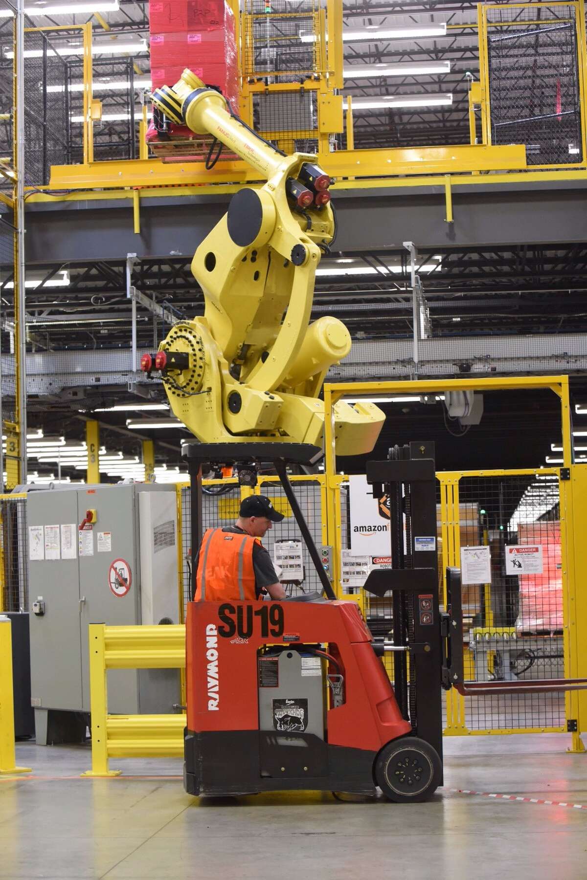 An Amazon employee works by a large robotic arm at the new Amazon Fulfillment Center in Schertz, Texas, on Friday, April 17, 2015.