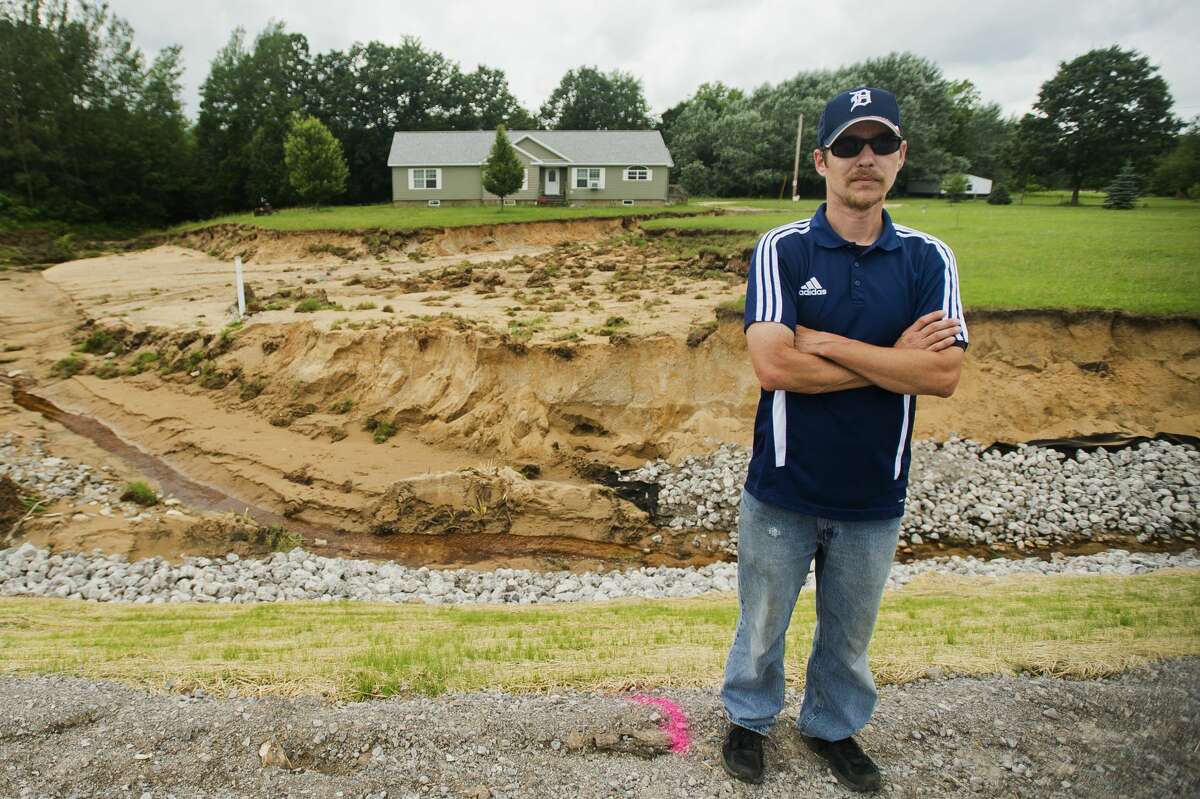 Billy Bryant poses for a portrait in front of the home he shared with his wife Kelly and son Gabriel, 11, before recent flooding washed away the majority of the front yard, as well as a basement wall and back porch, on Thursday, July 13, 2017 on Coleman Road near M-20.