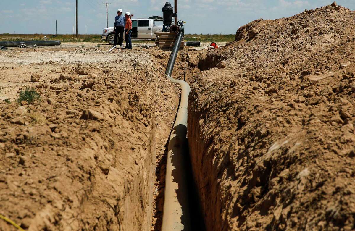 Layne Christensen principal business development engineer Byron Bevers, left, and business developer Tim Patrick stand next to a lay flat hose that connects a water well to their new pipeline Tuesday, July 18, 2017 in Pecos. The Woodlands based company is building a facility to supply water for hydraulic fracturing operations in the Delaware Basin. ( Michael Ciaglo / Houston Chronicle )