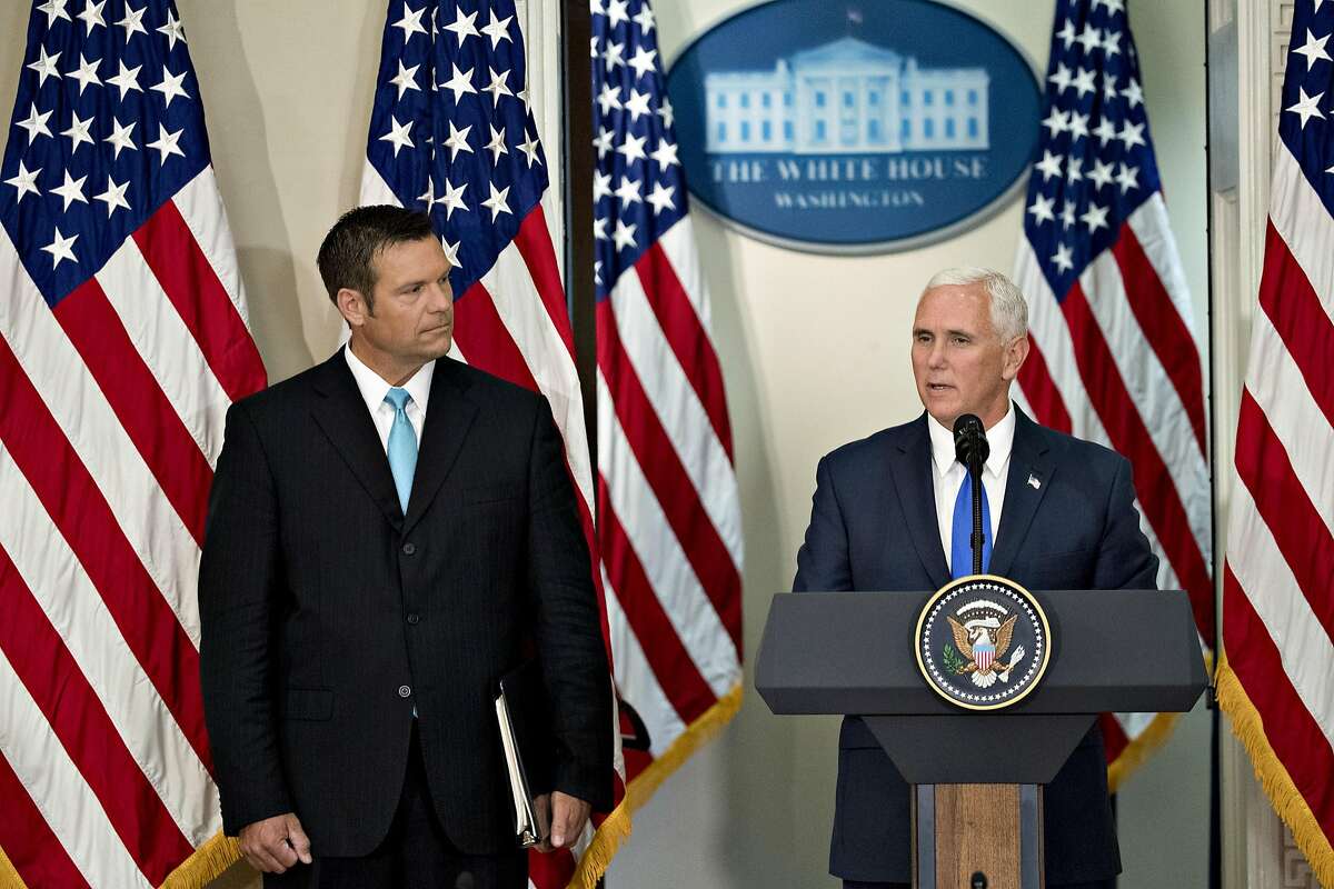 U.S. Vice President Mike Pence speaks as Kris Kobach, Kansass secretary of state, left, listens during the initial meeting of the Presidential Advisory Commission on Election Integrity at the Eisenhower Executive Office Building in Washington, D.C., U.S., on Wednesday, July 19, 2017. President Trump created the advisory commission in May, after claiming without evidence that 3 million people or more illegally voted for Hillary Clinton last year. Photographer: Andrew Harrer/Bloomberg