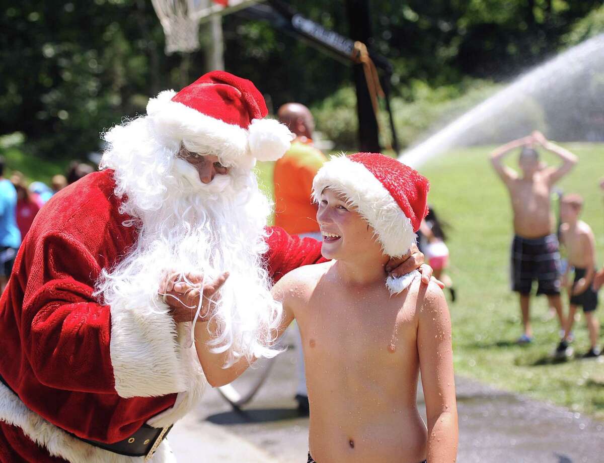 Boys and Girls Club of Greenwich camper Jake Romanello, 12, shakes hands with Santa during the annual Christmas in July event at Camp Simmons, Greenwich, Conn., Friday afternoon, July 21, 2017. The event has been taking place for almost two decades and courtesy of the Greenwich Fire Department, Santa arrives on a Greenwich fire truck, tosses candy canes to campers and then cools them down with water from a fire hose.