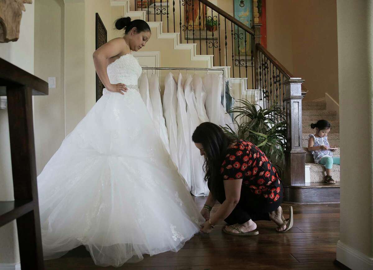 Monica Narvaez checks the bottom of Marcela Trejo's wedding dress during a fitting on Friday in Tomball. Trejo was able to get her dress for her July 29 wedding out of Alfred Angelo's store before it closed.