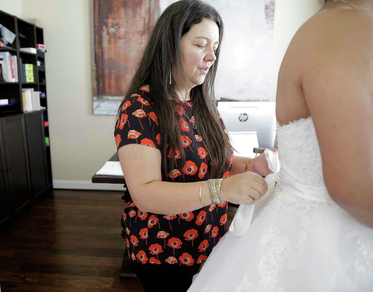 Monica Narvaez helps bride-to-be Marcela Trejo into her dress on Friday, July 21, 2017, in Tomball. Narvaez took 30& dresses from Alfred Angelo's three Houston stores before they shut down with a days notice. Narvaez, who hadn't been paid for the last two weeks, is doing the alterations, most of which the brides had already paid the bridal shop for. ( Elizabeth Conley / Houston Chronicle )