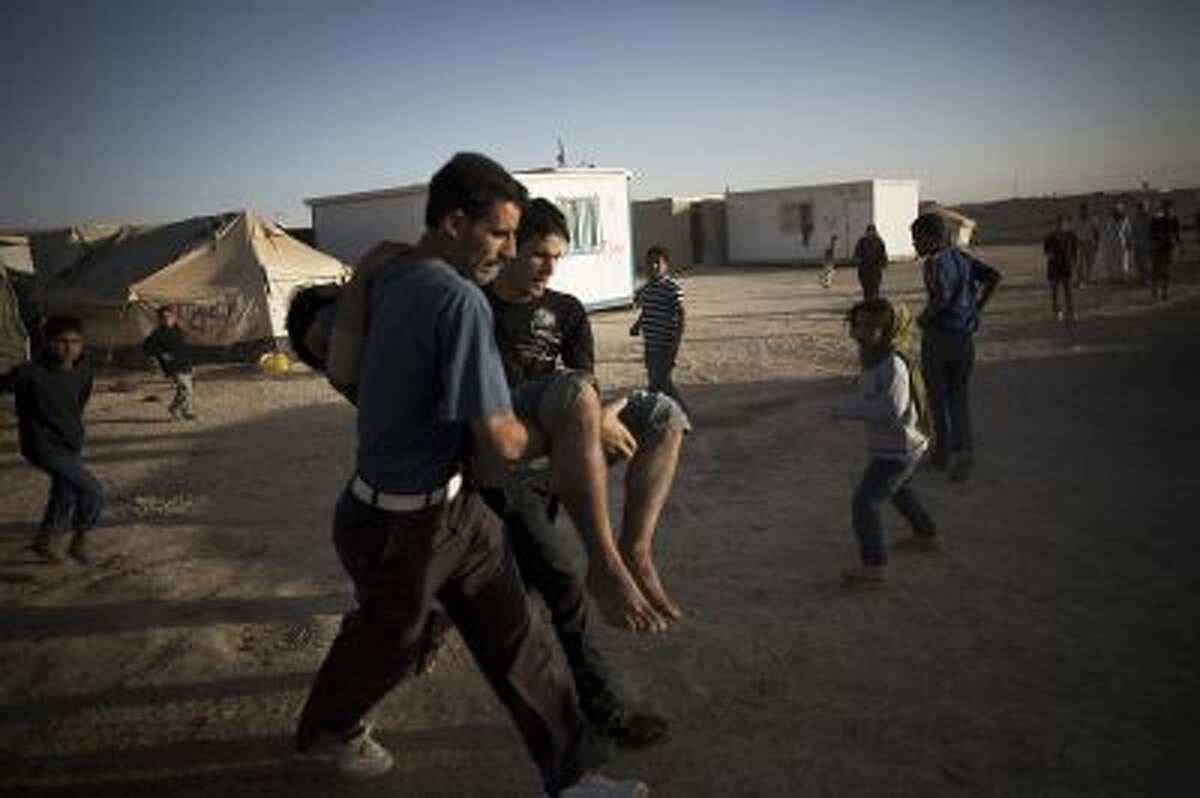 In this Tuesday, Oct. 22, 2013, photo, Syrian refugees carry a man who was wounded by a gas explosion during a fire at the Zaatari refugee camp near the Syrian border in Jordan. With Syrias civil war in its third year, more than 2 million Syrians have fled their country. About 100,000 live in this camp. (AP Photo/Manu Brabo)