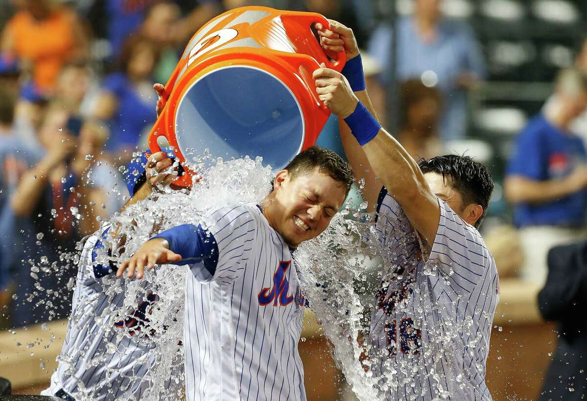 NEW YORK, NY - JULY 22: Wilmer Flores #4 of the New York Mets is doused with water by teammates T.J. Rivera #54 and Travis d'Arnaud #18 after his ninth inning game winning home run against the Oakland Athletics at Citi Field on July 22, 2017 in the Flushing neighborhood of the Queens borough of New York City. (Photo by Jim McIsaac/Getty Images) ORG XMIT: 700011714
