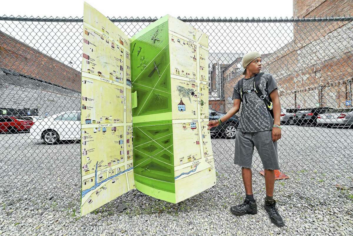 New Light High School senior Tyriq Banks, 17, positions a folding series of panels depicting the New Haven Green as a public art installation on Chapel Street in New Haven on Friday. Banks worked on the design and painting of the panels.