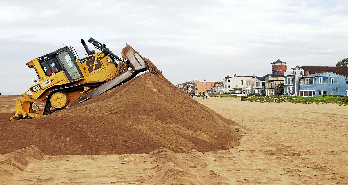 In this 2015 file photo, a bulldozer piles sand into a high berm to protect homes along Sunset Beach in Huntington Beach, Calif. The state’s Ocean Protection Council decided weeks ago to update its sea-rise guidance for state and local governments.