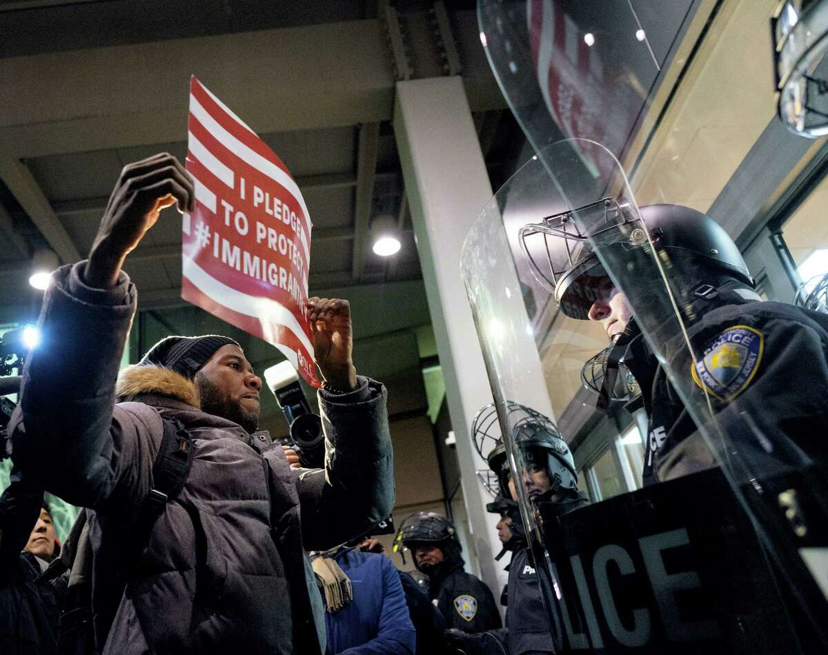 A protester stands facing police officers at an entrance of Terminal 4 at John F. Kennedy International Airport in New York, Saturday after earlier in the day two Iraqi refugees were detained while trying to enter the country. On Friday, Jan. 27, President Donald Trump signed an executive order suspending all immigration from countries with terrorism concerns for 90 days. Countries included in the ban are Iraq, Syria, Iran, Sudan, Libya, Somalia and Yemen, which are all Muslim-majority nations.