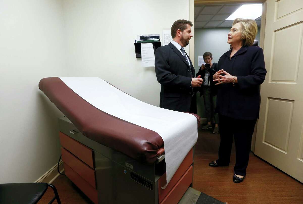 In this May 2, 2016 photo, Democratic presidential candidate Hillary Clinton listens to Dr. Christopher Beckett, CEO of Williamson Health and Wellness Center during a tour an exam room of the facility in Williamson, W.Va.
