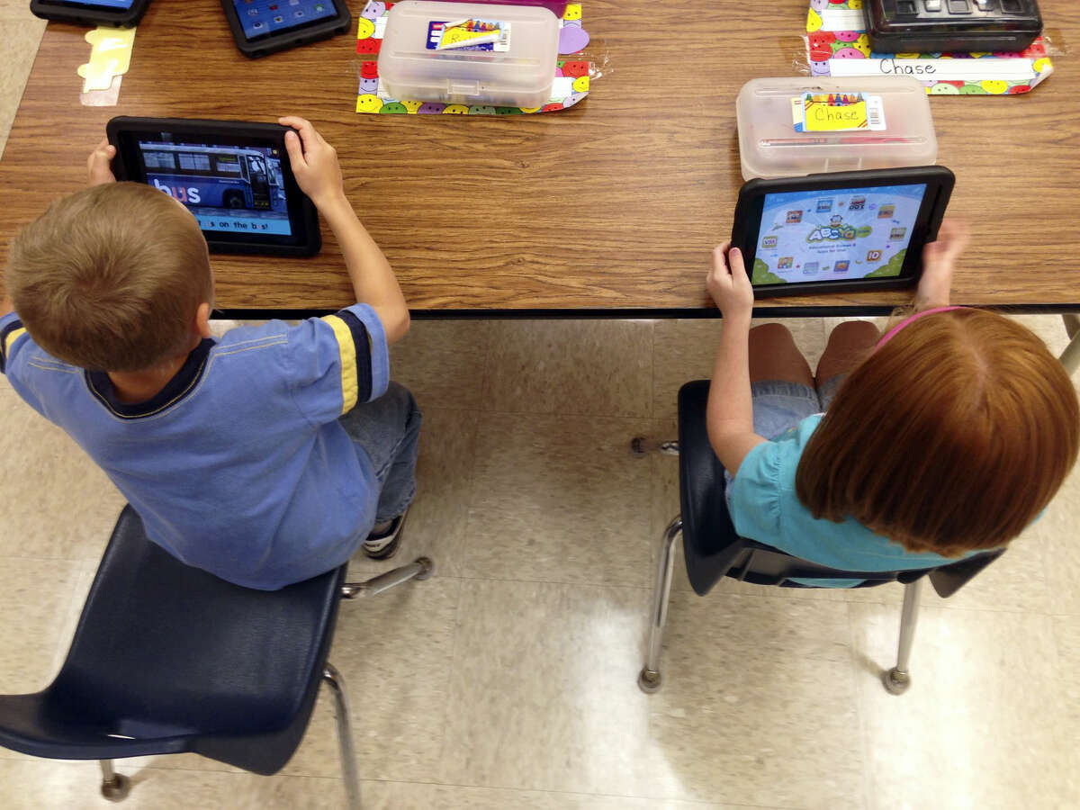 Two students do activities on iPads in a classroom.