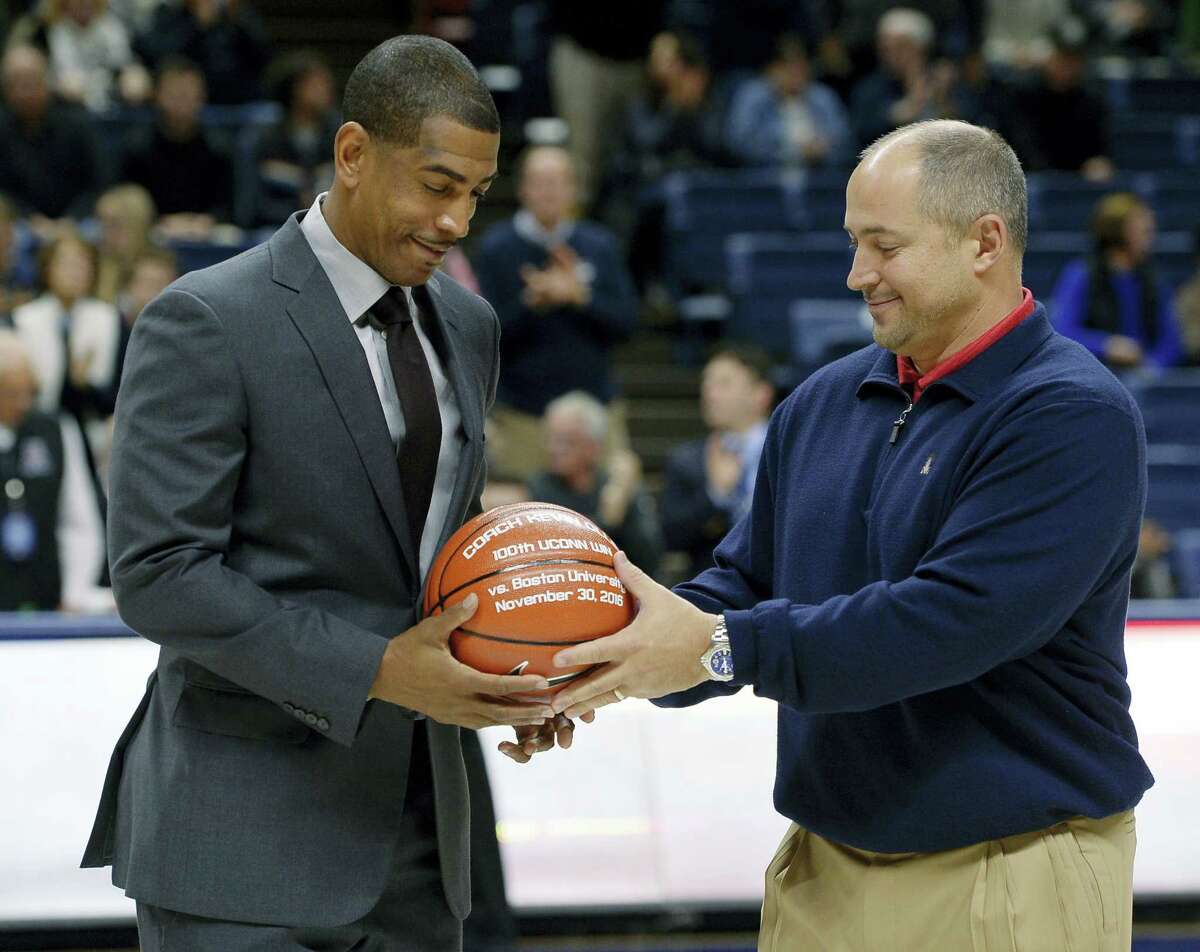 UConn head coach Kevin Ollie, left, is given a ball by athletic director David Benedict to honor his 100th win before Sunday’s game in Storrs.