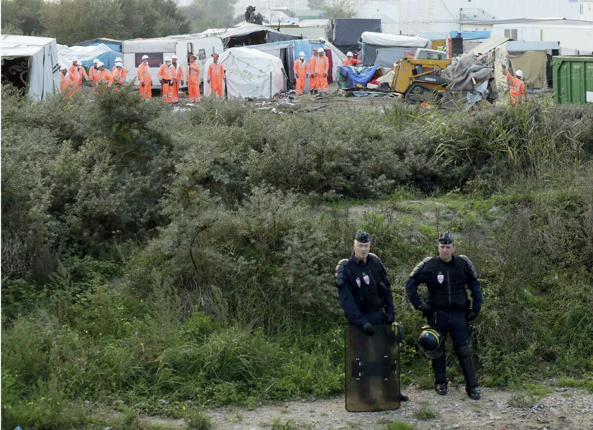 Riot police take position while crews start to demolish shelters, background, in the makeshift migrant camp known as “the jungle” near Calais, northern France, Tuesday, Oct. 25, 2016. Crews in hard hats and orange jumpsuits on Tuesday started dismantling a makeshift camp in France that has become a symbol of Europe’s migrant crisis while thousands of people remained there, waiting to be relocated.