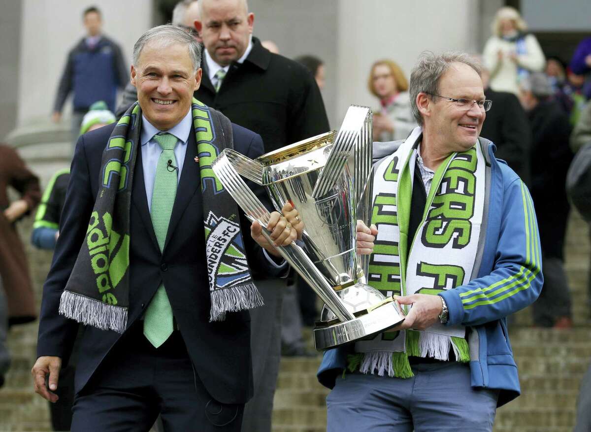 Seattle Sounders head coach Brian Schmetzer carries the MLS Cup trophy as he walks with Washington Gov. Jay Inslee, Wednesday in Olympia, Wash.