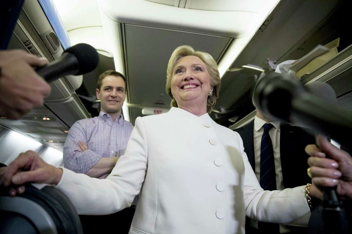 Democratic presidential candidate Hillary Clinton, center, accompanied by Campaign Manager Robby Mook, left, and traveling press secretary Nick Merrill, right, smiles as she speaks with members of the media aboard her campaign plane at McCarran International Airport in Las Vegas on Oct. 19, 2016 following the third presidential debate.