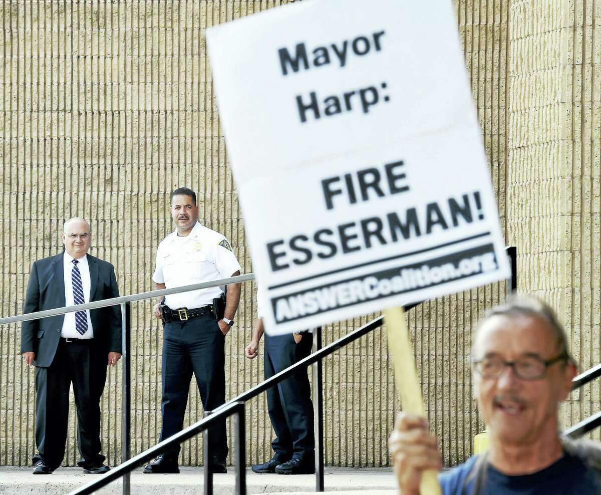 From left, Assistant Chiefs Achilles “Archie” Generoso and Luiz Casanova watch Norman Clement and others protest against New Haven Police Chief Dean Esserman in front of the New Haven Police Department Tuesday.