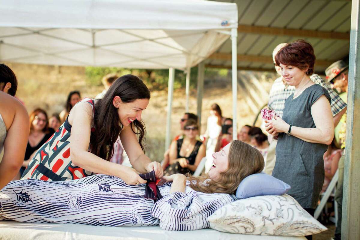 Amanda Friedland, left, surrounded by friends and family, adjusts her friend Betsy Davis’ sash as she lies on a bed during her “Right To Die Party.”