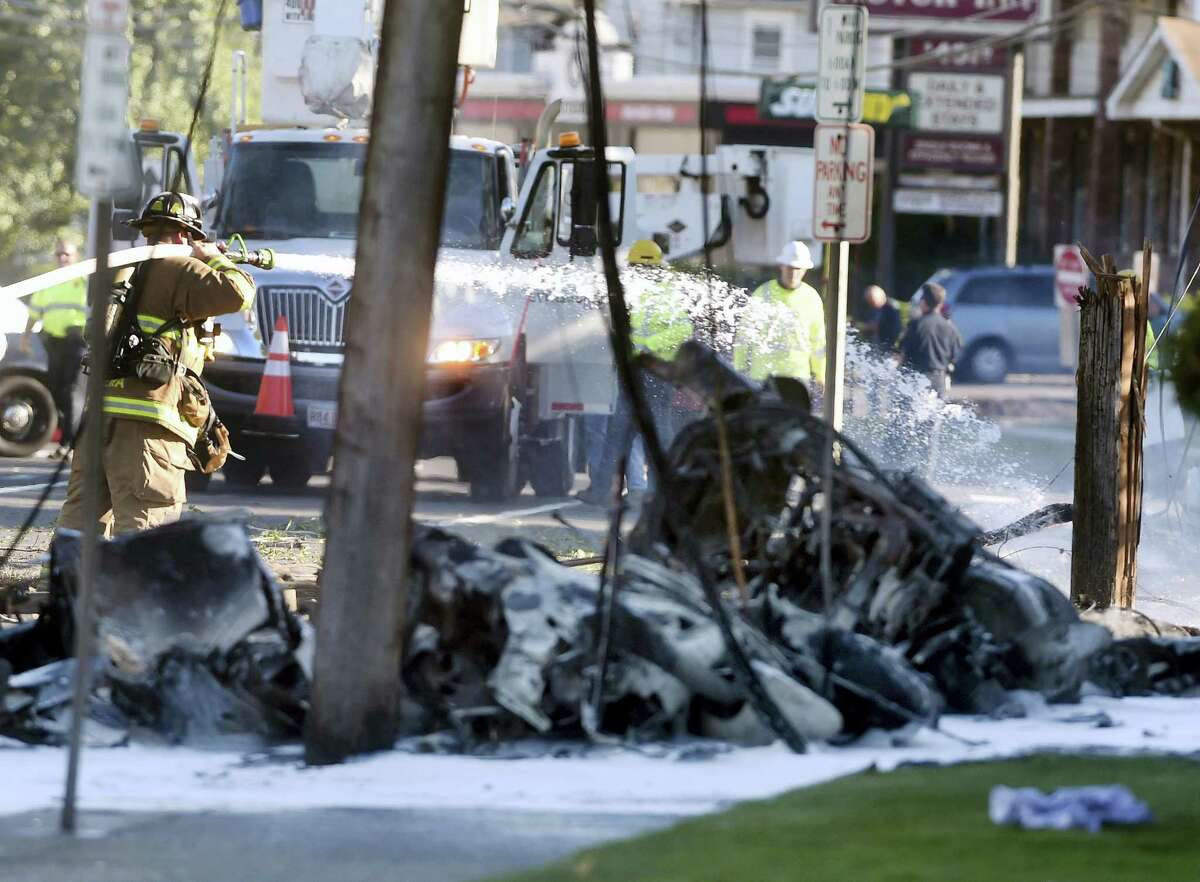 Firefighters use foam to extinguish the fire of a demolished aircraft after the plane crashed on Main Street in East Hartford on Tuesday. Authorities said at least one person is dead and another is injured after a small airplane crashed near the Connecticut River. Jim Michaud — Journal Inquirer via AP)
