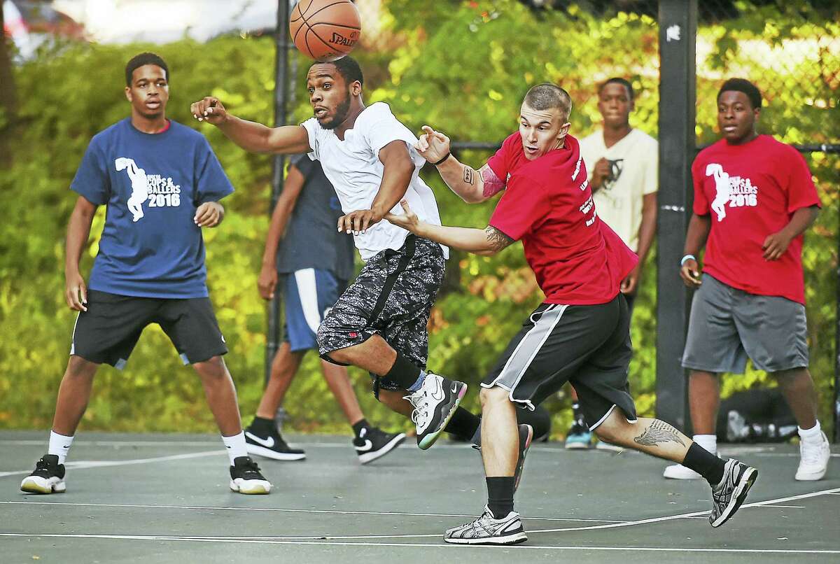 Warren Ligon, second from left, in white, and Officer Marco Correa, third from left, battle for a rebound at the “Cops and Ballers” community basketball tournament Wednesday at Edgewood Park in New Haven.