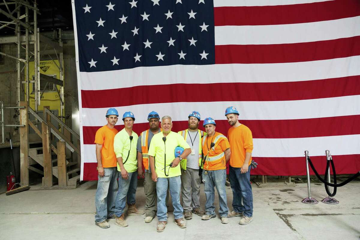 Construction workers pose for photos in front of the United States flag before a topping off ceremony for 3 World Trade Center on June 23, 2016 in New York. It’s one of three new skyscrapers that replace the twin towers destroyed almost 15 years ago.