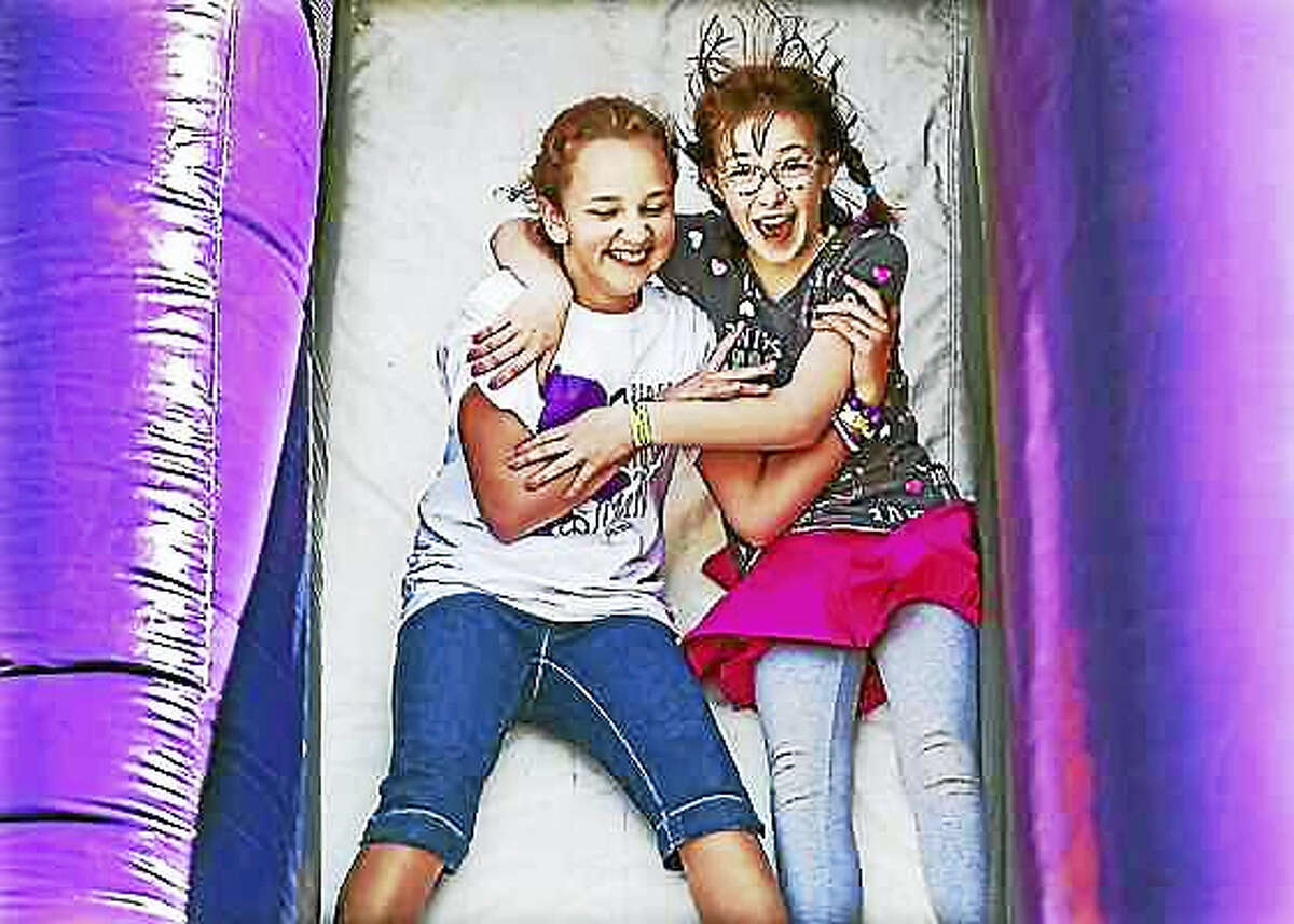 Natalie Raynor, 10, at left, and her new friend, Annabelle Farrell, 11, make their way down an inflatable purple slide, arm in arm, meeting for the first time at “Peace, Love & Music from Maren,” April 25, 2015, at Jonathan Law High School.