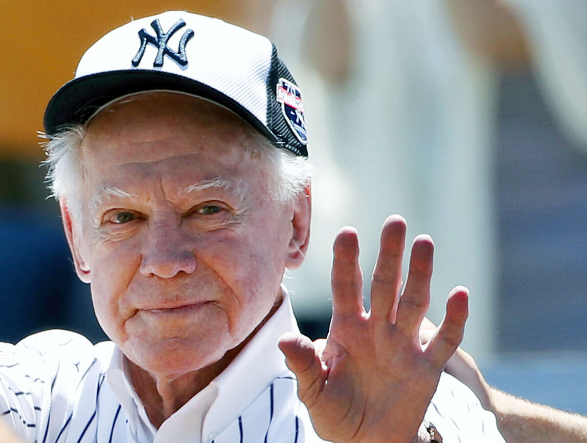 Former Yankees pitcher Whitey Ford waves to fans from outside the dugout.