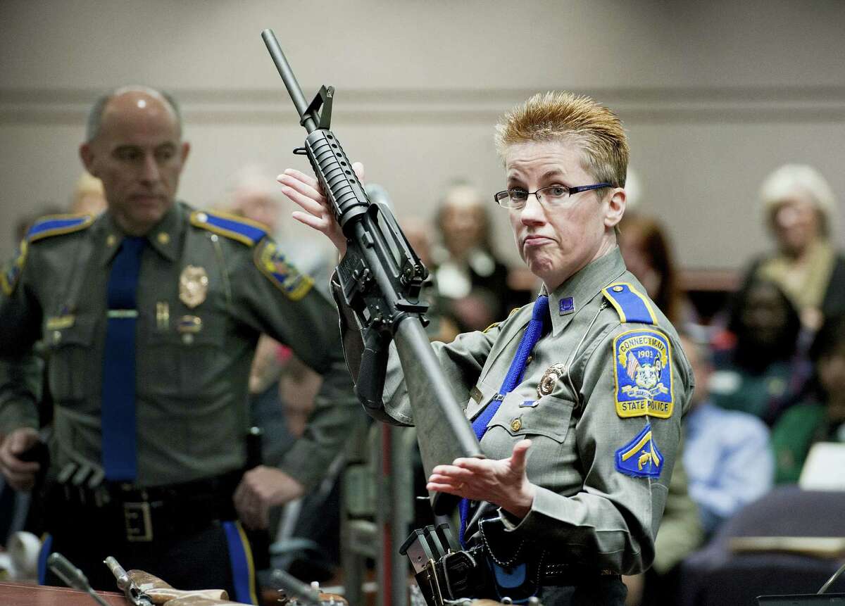 In this Jan. 28, 2013 photo, firearms training unit Detective Barbara J. Mattson, of the Connecticut State Police, holds up a Bushmaster AR-15 rifle, the same make and model of gun used by Adam Lanza in the Sandy Hook School shooting, during a hearing of a legislative subcommittee, at the Legislative Office Building in Hartford, Conn. Lawyers for the company that made the rifle Lanza used at Sandy Hook Elementary School in 2012 are expected to ask a Connecticut judge on Monday, Feb. 22, 2016 to dismiss a wrongful death lawsuit filed by families of some of the massacre victims.