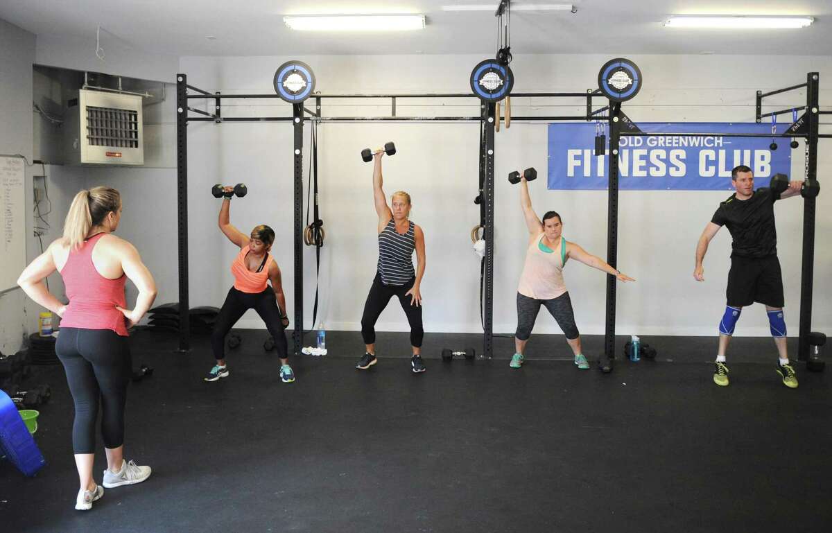 Group fitness instructor Chrissy Linegar, far left, observes as class participants, from left, Sue Aarons, Wendy Putnam, Paige Elgarten, and Dave Glass perform overhead dumbbell lifts in a group circuit workout at Old Greenwich Fitness Club in Old Greenwich, Conn. Thursday, July 20, 2017. Several former members of the Crossfit gym formerly at the location rebranded and renovated the facility to make it more family friendly.