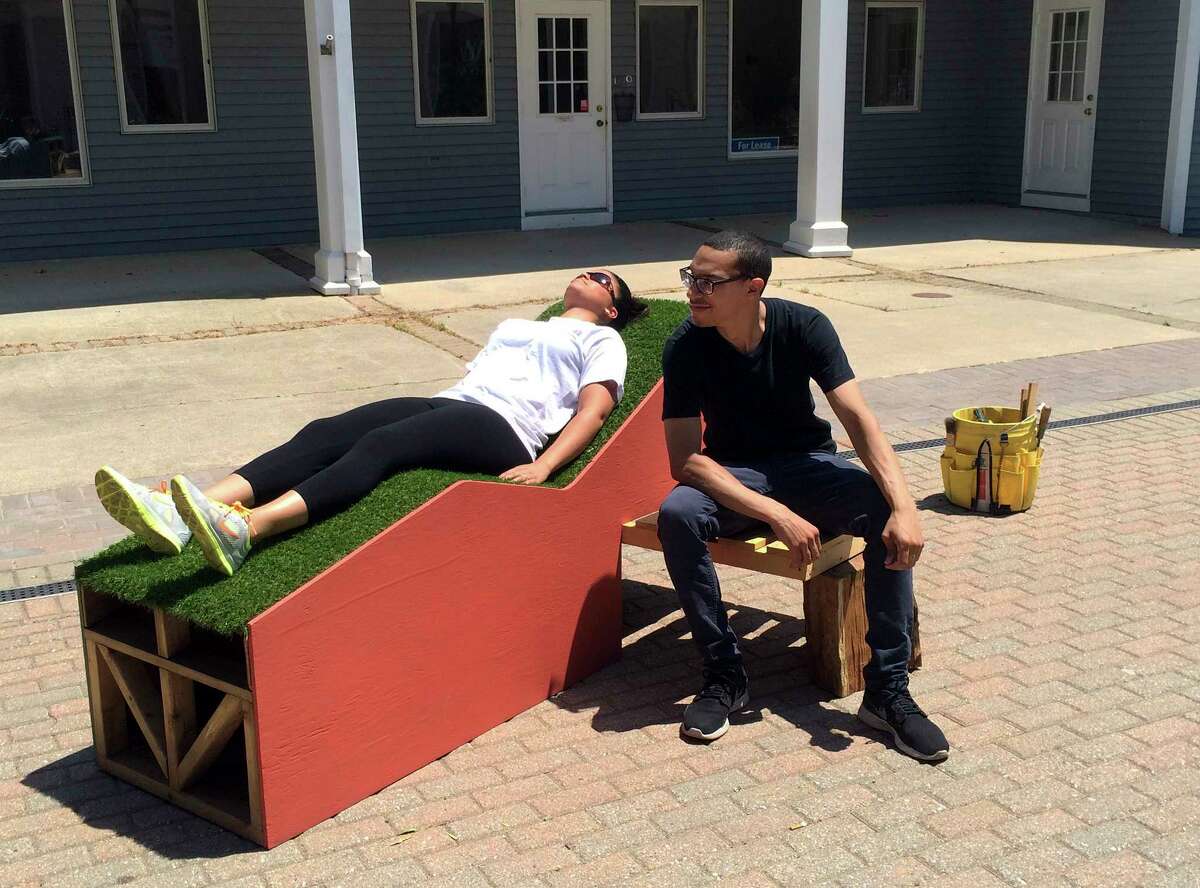 In this Sunday, June 14, 2015 photo provided by New York City artist Jim Osman, his assistant Alex Reyes, right, sits beside a passer-by lying on the wood and tile "Corbu Bench" sculpture that Osman installed in Madison, Conn., as part of the townís 15th annual Sculpture Mile event. The sculpture was torn apart and put in a dumpster soon after the installation on Sunday by a maintenance worker, believing it was not allowed in the plaza. (Jim Osman via AP)
