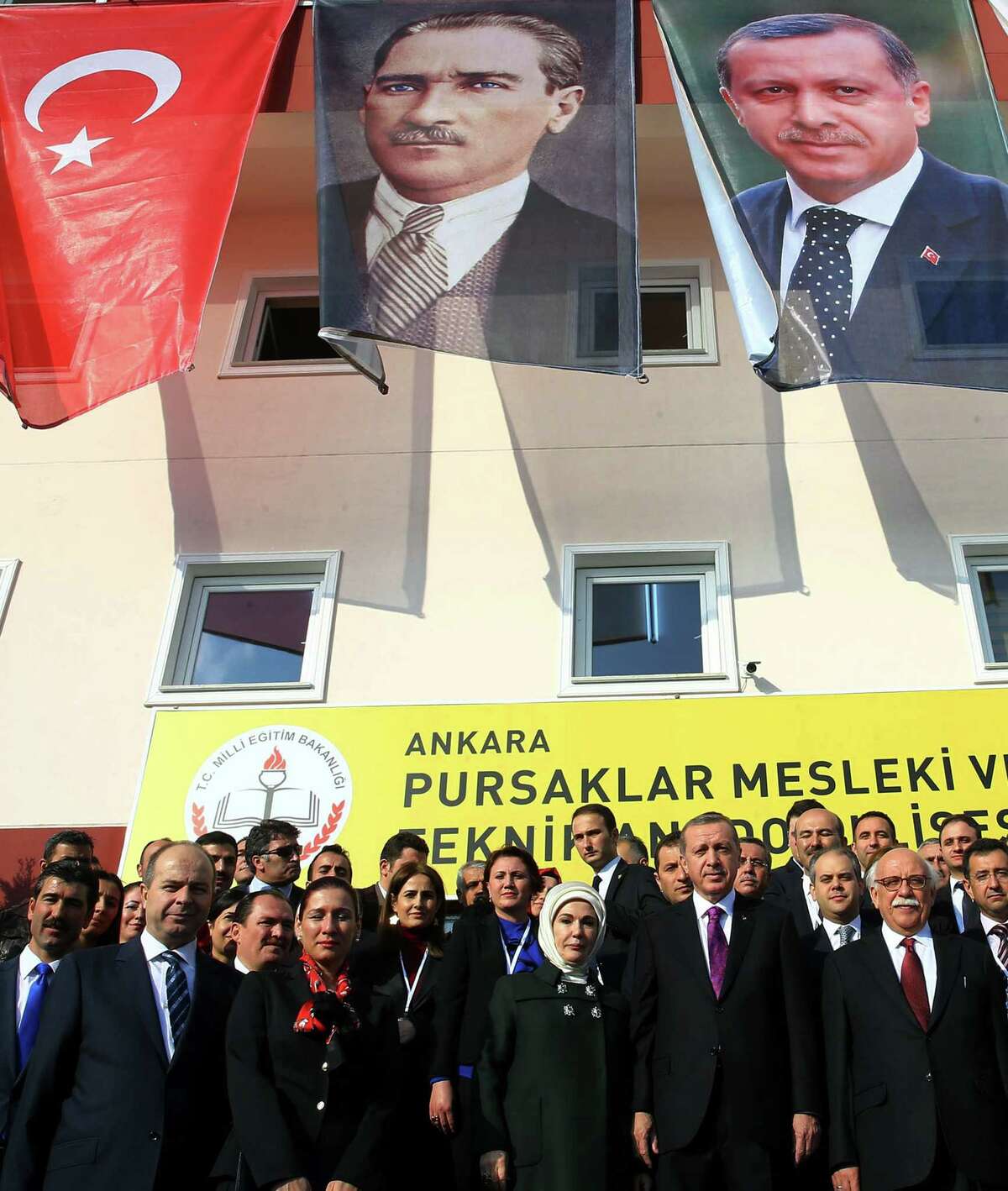 FILE - In this Nov. 18, 2014 file photo, Turkish President Recep Tayyip Erdogan, center-right, and his wife Emine Erdogan pose for photos with officials in the courtyard of a Vocational School for Girls under a poster of Mustafa Kemal Ataturk, center, outside Ankara, Turkey. Turkey has long enshrined the secular ideals of founding father Mustafa Kemal Ataturk, particularly in an education system in which Islamic headscarves were until recently banned in schools and schoolchildren began the day reciting an oath of allegiance to Ataturkís legacy. Now proponents of Turkeyís secular traditions claim President Recep Tayyip Erdogan is overturning those traditions by building a more Islam-focused education system to realize his stated goal of raising ìpious generations.î (AP Photo/File)