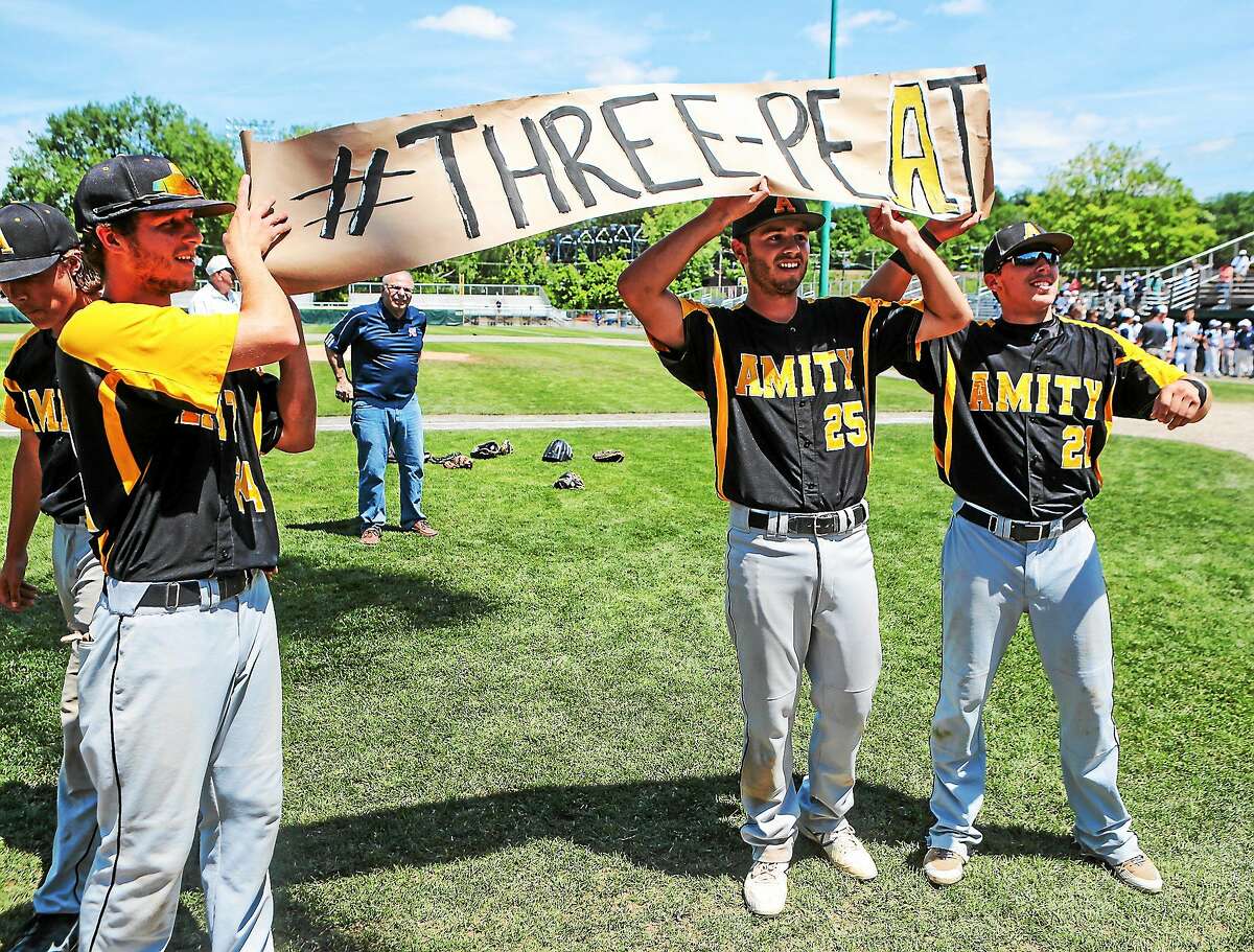 Kyle Mattei (left), Amity’s baseball players hold up a “THREE-PEAT” sign following their third-consecutive Class LL baseball championship, 8-1 over Staples.