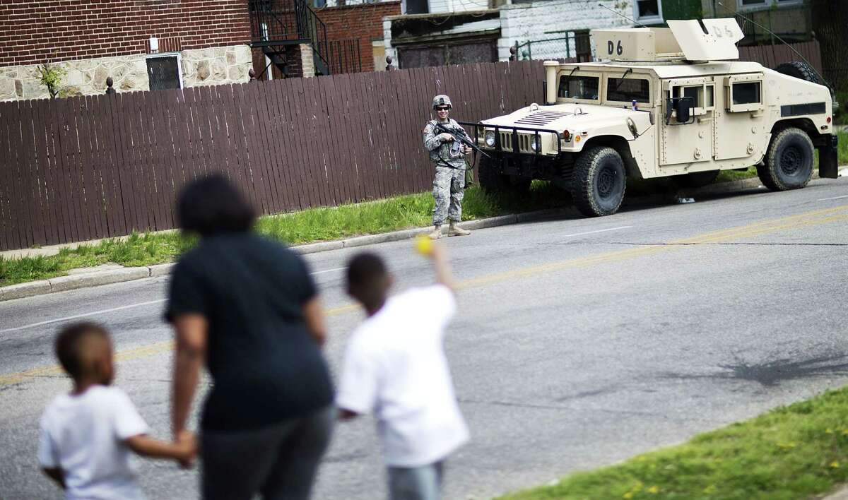 A member of the National Guard stands watch outside a neighborhood next to the Mondawmin Mall following Freddie Gray’s funeral, as a mother passes with her children.