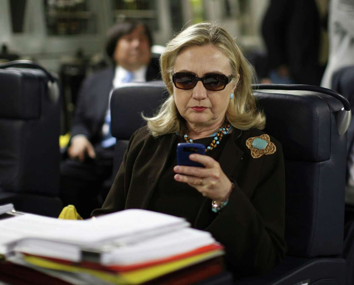In this Oct. 18, 2011, file photo, then-Secretary of State Hillary Rodham Clinton checks her Blackberry from a desk inside a C-17 military plane upon her departure from Malta, in the Mediterranean Sea, bound for Tripoli, Libya.