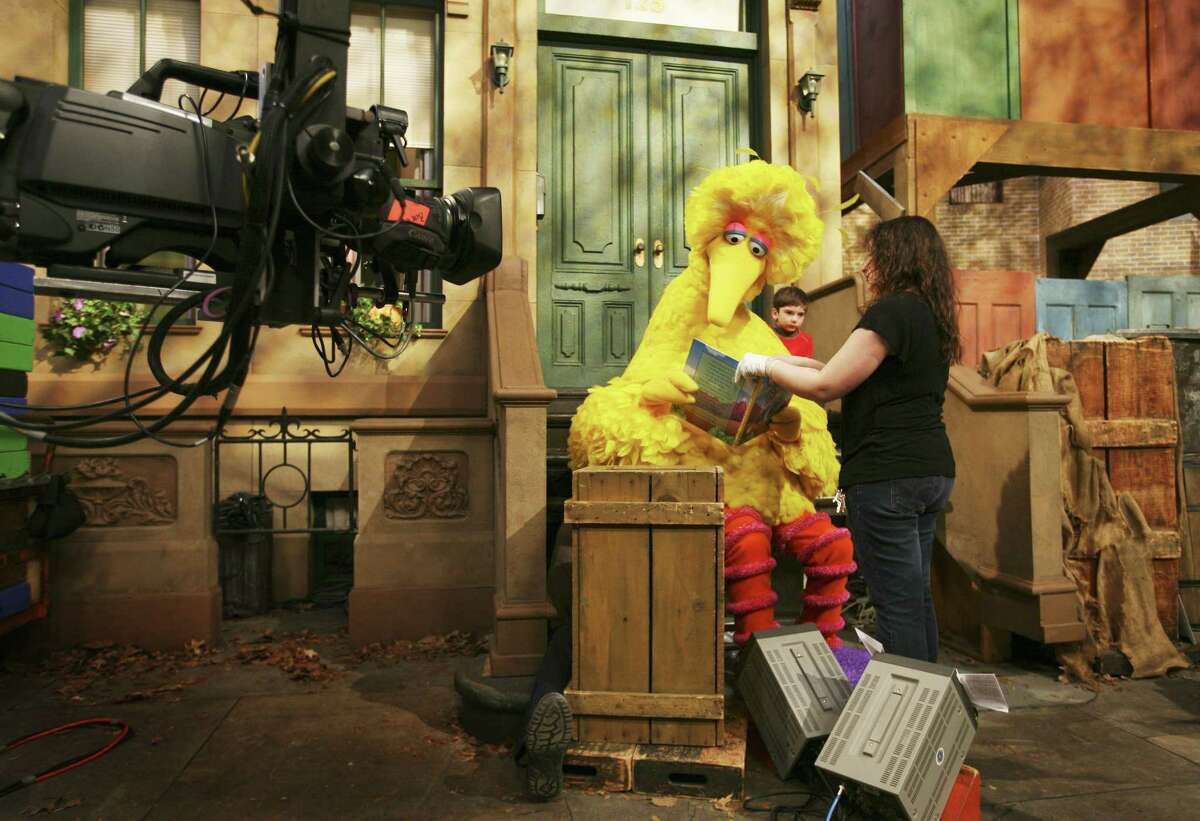 In this 2008 file photo, Michelle Hickey, a Muppet wrangler adjusts a book for Big Bird, voiced by Carroll Spinney, so he can read to Connor Scott during a taping of Sesame Street in New York.