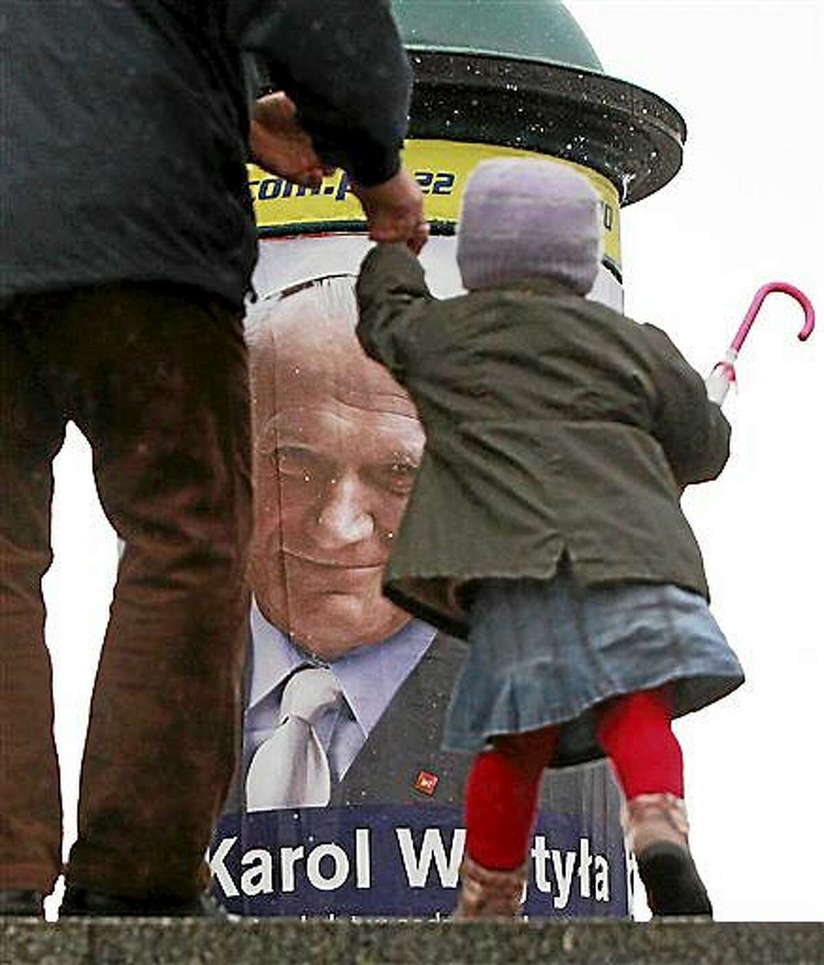 A pedestrian leads a child by a poster in Warsaw marking 10 years since the death of Polish-born Pope John Paul II. The poster encourages people to make their daily decisions in accordance with his teachings. John Paul will be gone a decade on Thursday. To attract attention to the poster, the pope, born as Karol Wojtyla, appears as a lay candidate in Poland’s May 10 presidential elections.