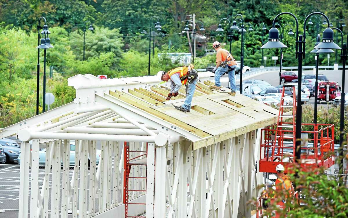 Richard Cyr, center, screws boards into place Tuesday on the roof of a pedestrian bridge that will cross over the railroad tracks at the Branford train station.