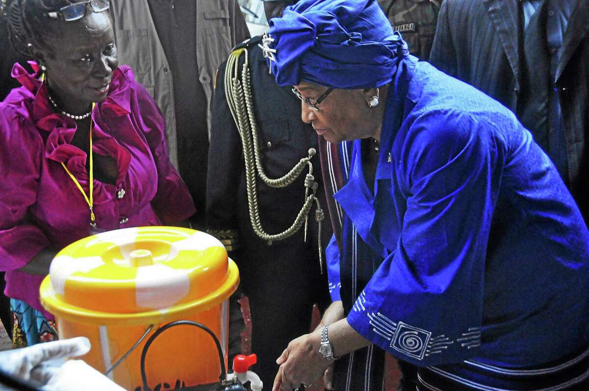 Liberian President Ellen Johnson Sirleaf, right, demonstrates to people how to wash their hands properly in order to prevent the spread of the Ebola virus.