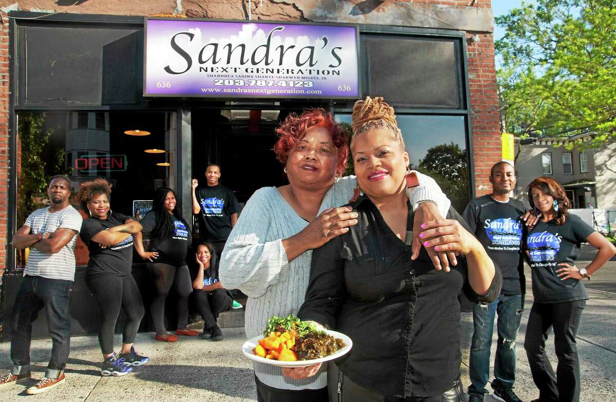 Mary Harris, left, and her daughter, Sandra Pittman, backed by friends, family and staff, in front of Sandra’s Next Generation Soul Food Restaurant on Congress Avenue in New Haven. Pittman is holding a plate of Go Green Chicken, sweet potatos and collard greens. The chicken is low sodium and flavored with herbs with no added salt.