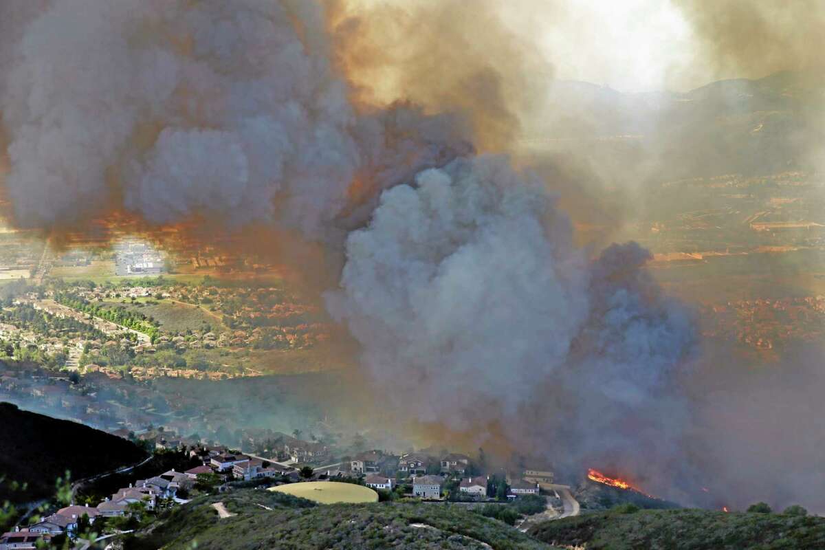 A wildfire approaches homes on May 14, 2014, in San Marcos, Calif. Flames engulfed suburban homes and shot up along canyon ridges in one of the worst of several blazes that broke out Wednesday in Southern California during a second day of a sweltering heat wave, taxing fire crews who fear the scattered fires mark only the beginning of a long wildfire season.