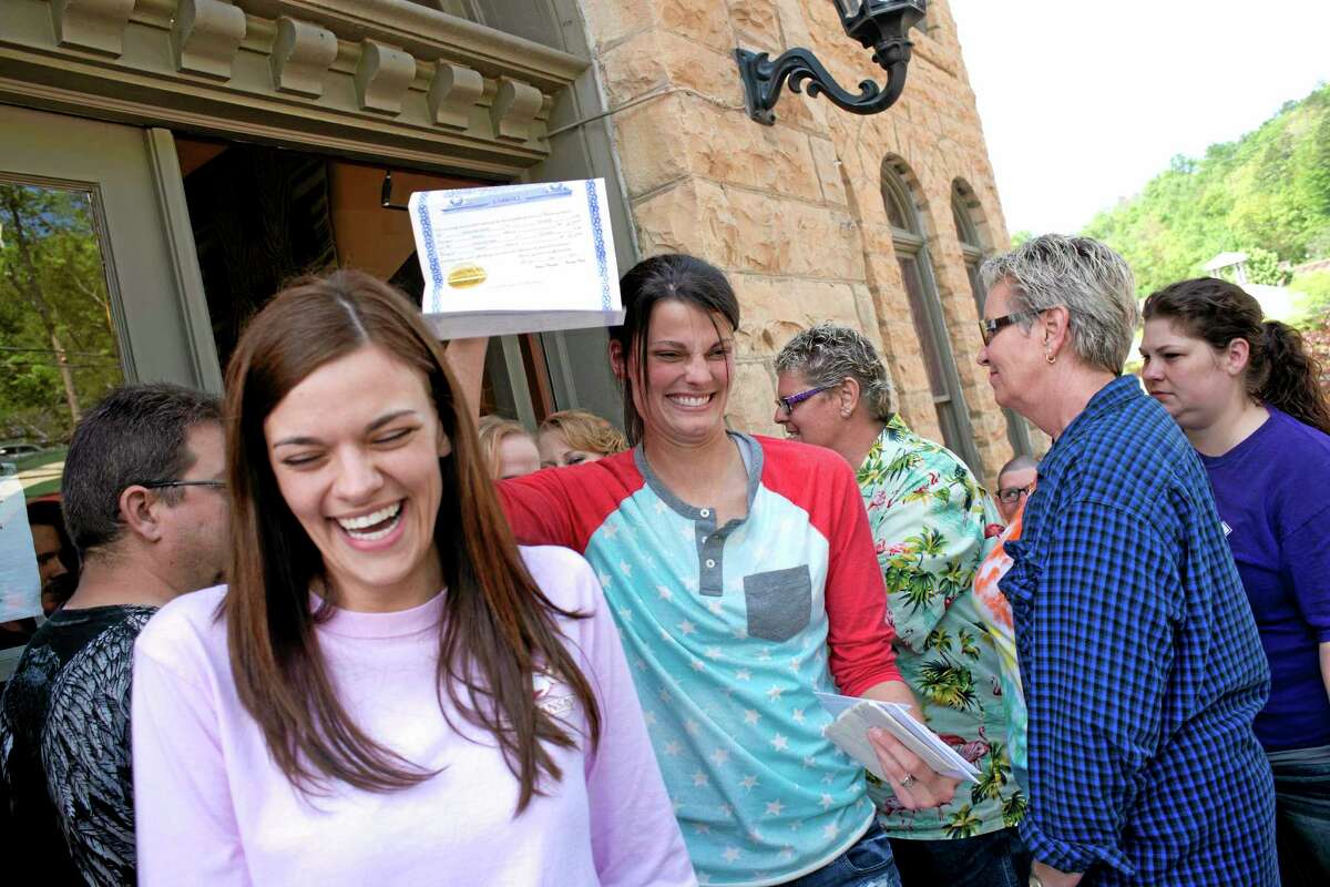 In this May 10, 2014, file photo, Kristin Seaton, center, of Jacksonville, Ark., holds up her marriage license as she leaves the Carroll County Courthouse in Eureka Springs, Ark., with her partner, Jennifer Rambo, left, of Fort Smith, Ark., in Eureka Springs, Ark. The Arkansas Supreme Court has rejected the state attorney general’s request for a stay of a judge’s ruling that overturned Arkansas’ constitutional ban on gay marriage, Wednesday, May 14, 2014.