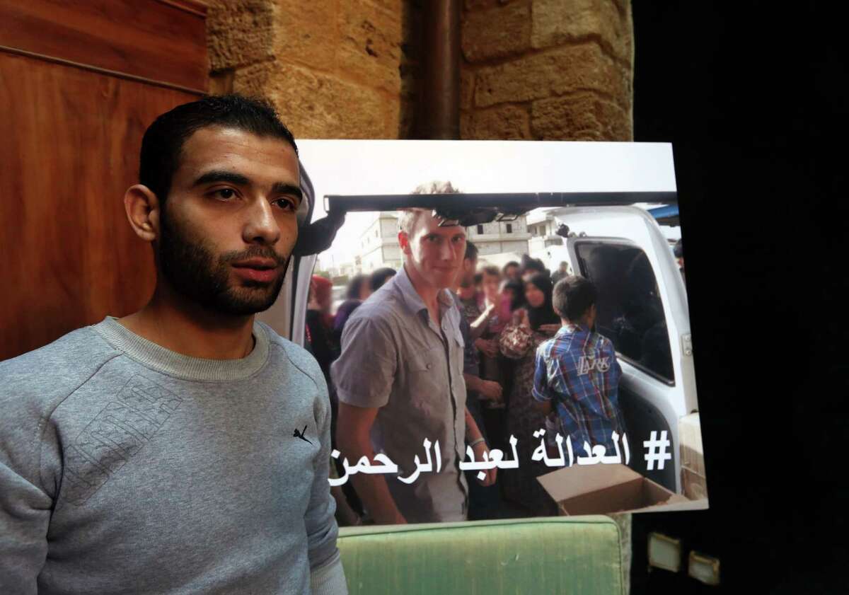 Syrian refugee Amjad Moghrabi stands in front of a photograph of his colleague, American aid worker Peter Kassig, 26, who converted to Islam while in captivity and changed his name to Abdul-Rahman Kassig, during an interview with The Associated Press in the northern port city of Tripoli, Lebanon, Saturday, Nov. 8, 2014. Kassig was helping victims of the Syrian civil war when he was captured in Syria last year and threatened with beheading by the Islamic State group. Arabic reads, "Justice for Abdul-Rahman." (AP Photo/Bilal Hussein)