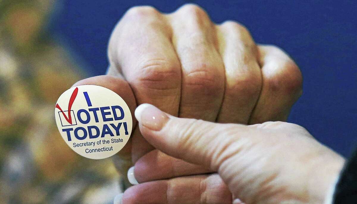 In this Nov. 6, 2012, file photo, poll worker Chris Theriot hands out an “I Voted Today!” sticker after a resident placed her ballot in the box at the North Street School in Greenwich.