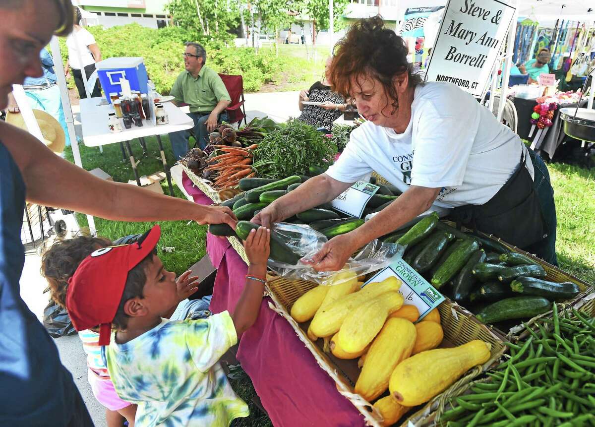 Talin Patel, 4, picks out a cucumber from Mary Ann Borrelli of Steve and Mary Ann Borrelli Farm in North Branford at the farmers market at 943 Dixwell Avenue in Hamden Monday. At left is Talin’s mother, Anna.