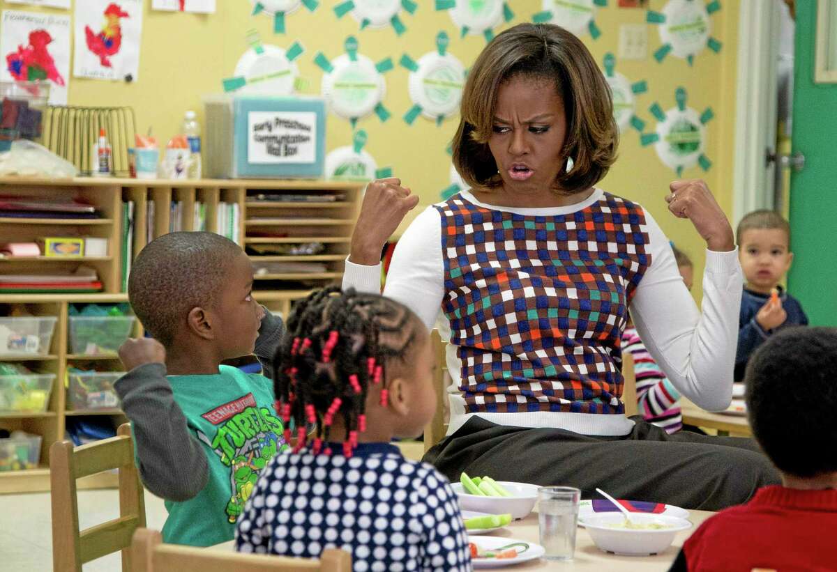FILE - In this Feb. 27, 2014 file photo first lady Michelle Obama and a young student show off their muscles as they eat healthy snacks during a visit to La Petite Academy in Bowie, Md., to encourage healthy habits at preschool as part of her Let's Move! Child Care program. First ladies typically avoid getting into public scraps, but Obama is in the biggest fight of her tenure as she pushes back against a House Republican effort to soften a key component of the anti-childhood obesity effort at the center of her legacy. And she says she is ready ìto fight until the bitter end,î if that is what it takes. (AP Photo/Carolyn Kaster, File)