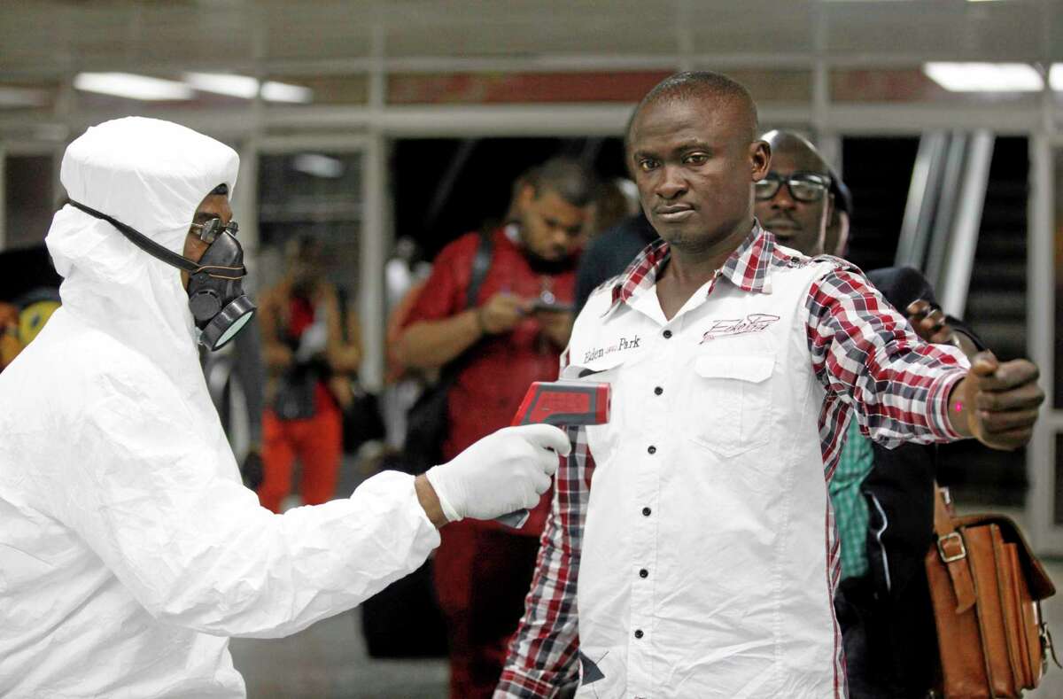 FILE - In this Aug. 6, 2014 file photo, a Nigerian port health official uses a thermometer on a worker at the arrivals hall of Murtala Muhammed International Airport in Lagos, Nigeria. As the Ebola outbreak in West Africa grows, airlines around the globe are closely monitoring the situation but have yet to make any drastic changes. (AP Photo/Sunday Alamba, File)
